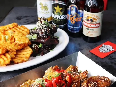 Platter of sesame-glazed Peking sticky wings with waffle fries and bottled Asian beers at The Peterboro in Detroit's Historic Chinatown