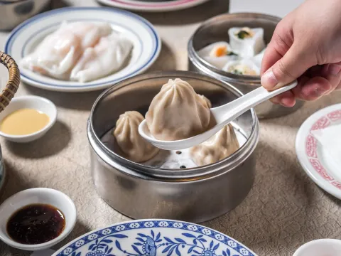 A steamed soup dumpling lifted with a spoon from a bamboo steamer basket at Nom Wah Tea Parlor